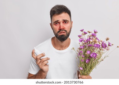 Pollen Allergy Concept. Unhappy Bearded European Man With Red Swollen Eyes Runny Nose Uses Medicament Against Allergy Suffers From Seasonal Allergic Rhinitis Isolated Over White Studio Background