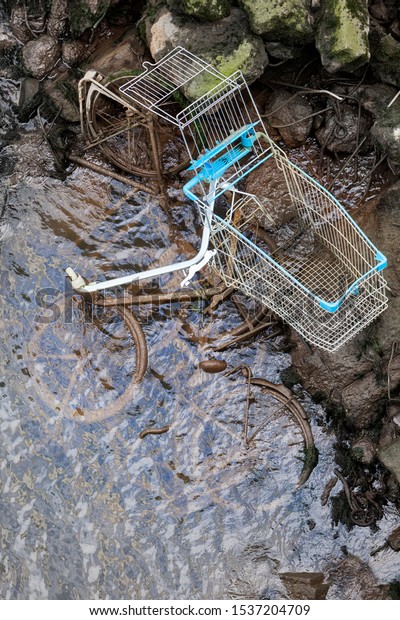 Pollution by dumped bicycles and a\
shopping cart at the edge of a river in the\
Netherlands