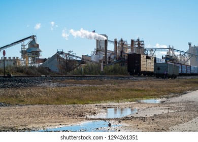 Pollution And Climate Change. Factory In Texas Producing Fossil Fuel Smoke Stack And Train Tracks Leading To Industrial Revolution Style. Water Puddles In The Foreground And Transportation