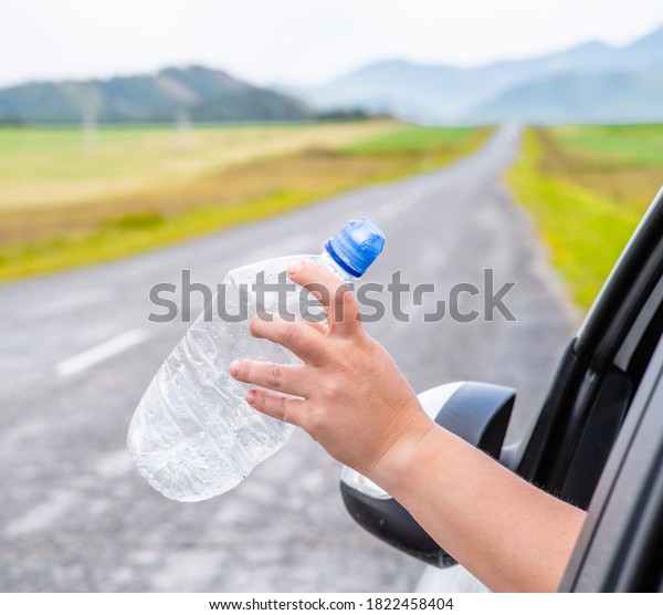 Pollution of nature concept. Driver\
throwing away plastic bottle from car window on the\
road