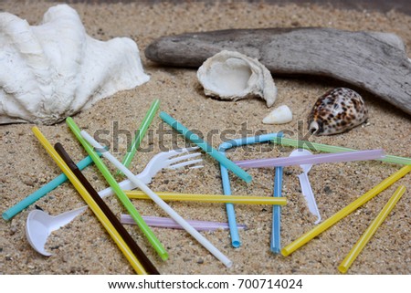 Pollution of plastic straws and fork left on beach background with beautiful seashells and drift wood.  Plastic pollution is harmful to  marine lives. Environmental concept. Ban single use plastic. 