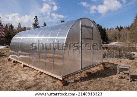 Polycarbonate greenhouse in the garden. The greenhouse is used for growing organic plants at home. Growing vegetables and fruits, gardening. The light is the setting bright sun.