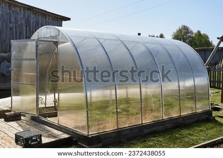A polycarbonate greenhouse stands on the plot