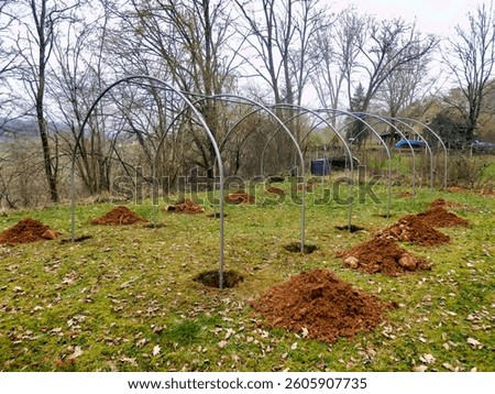 Polytunnel under construction - Polytunnel hoops connected to ridge bar and assembled on to the base plates buried in the ground
