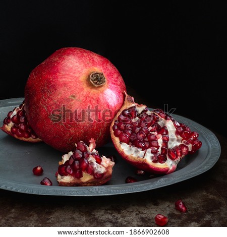 Pomegranate fruit whole and open on a silver platter and black background, square