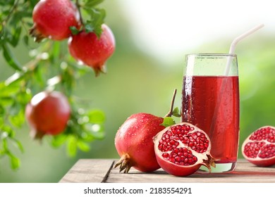 Pomegranate juice with fresh fruits on wooden table with pomegranate plant background.