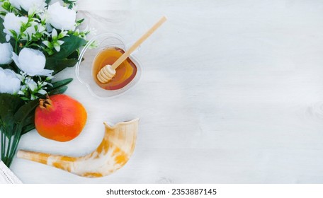 pomegranate, rimmon, Honey and white flowers and shofar on a white white wooden background . A symbol of the Rosh Hashanah holiday. Suitable for shana tova greeting card. with free space for text 