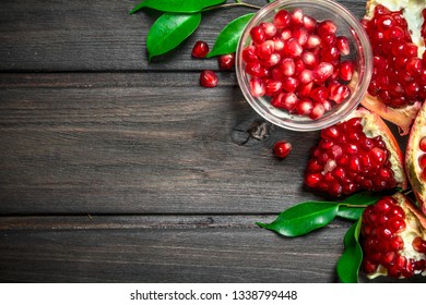 Pomegranate seeds in a bowl and pieces of ripe pomegranate with leaves. On wooden background - Shutterstock ID 1338799448