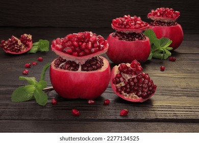 The pomegranate is sliced ​​in the shape of a sombrero. Juicy, ripe, red pomegranate on a wooden, black, old table, beautifully decorated and close-up shot. Pomegranate pieces are surrounded by pomegr