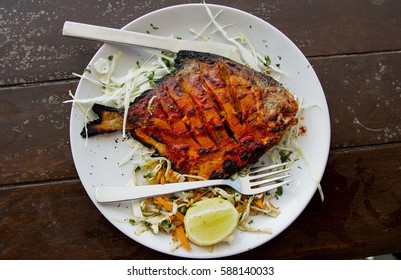 Pomfret fish cooked in a clay oven (tandoor) garnished with lemon on a white plate and a brown wooden table in north Goa's Baga beach