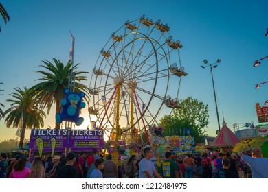 Pomona, California USA - September 23rd, 2018. Many People Walking In LA County Fair With Ferris Wheels Against Sunset Blue Sky Background. 