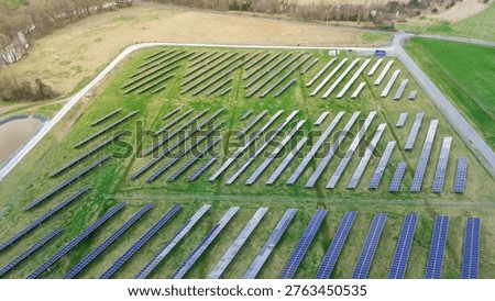 Pond side solar array lies near Creamery Road within Emmitsburg industrial corridor. Reflective panels, grassy lanes, small water feature create balanced geometric renewable energy textures, MD. USA