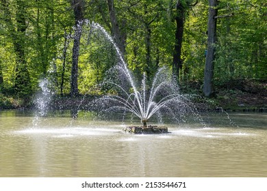 Pond with a working fountain with jets of water coming out and falling on the water, lush green trees in the background, sunny spring day in Heidekamp park in Stein, South Limburg, Netherlands - Shutterstock ID 2153544671