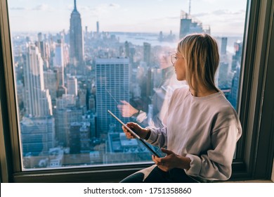 Pondering Millennial Blogger Holding Modern Digital Tablet And Dreaming During Travel Journey In New York Looking On Manhattan District From Above, Youthful Woman With Technology Thinking Indoors