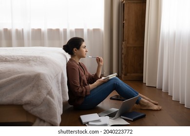 Pondering on answer. Pensive young indian female student sit on floor at bedroom prepare coursework write essay use laptop paper literature. Thoughtful millennial hindu lady do paperwork create idea