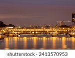 The Pont de Bercy and Passerelle Simone de Beauvoir over the Seine River in Paris illuminated at twilight, their lights reflecting on the water