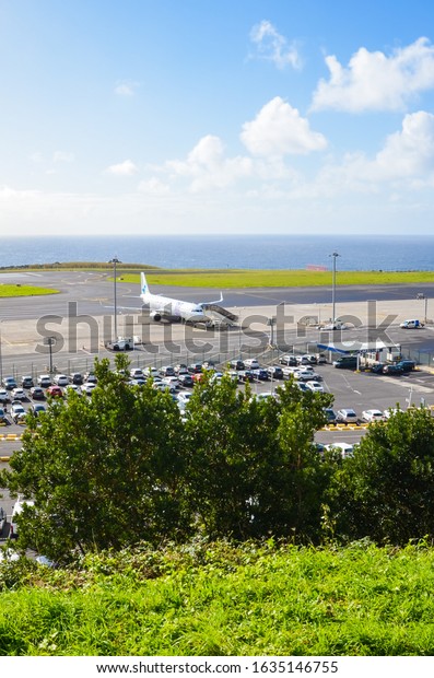 Ponta Delgada, Azores, Portugal - Jan 14,\
2020: View of Joao Paulo II Airport in Sao Miguel Island. Runway\
with a plane, building of the terminal and parking lot for rental\
cars. Ocean in\
background.