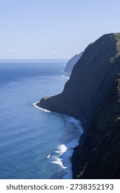 Ponta do Pargo Atlantic cliffs Madeira Portugal vertical view, towering green escarpments drop into calm blue ocean with curving surf lines distant horizon and clear daylight sky