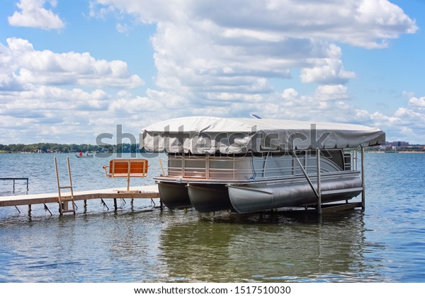 Pontoon boat with cover resting on a boat lift on an\
inland lake