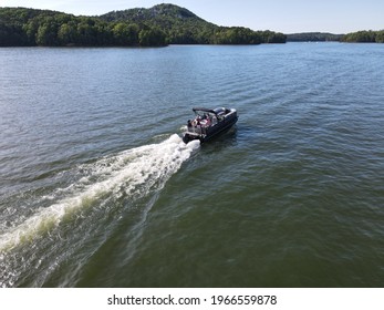 Pontoon boat cruising in open water on lake. Lake is surrounded by trees