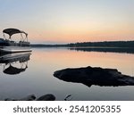 pontoon boat and trees reflecting on a still body of water after sunset