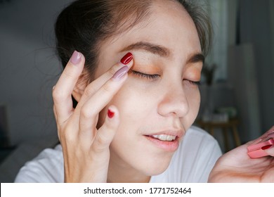 Ponytail woman joyfully applying eye shadow on her eyelid with fingers with nail painting.