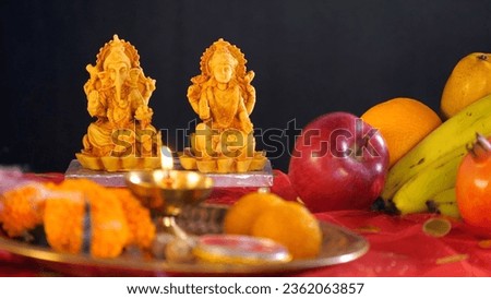 Pooja Thali with a Diya, marigold flowers, and sweets - Worshipping Indian Gods. Closeup shot of Hindu God statues of Lord Ganesha, Ma Lakshmi with fruits like apples, bananas, and oranges