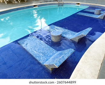 Pool with blue tiles and a table with two chairs. The pool is surrounded by a white fence