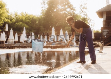 Pool cleaner is scooping leaves from the pool surface and talking on the phone at the same time in a luxury resort