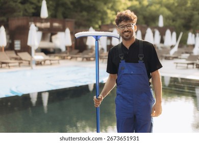 Pool cleaner in uniform, smiling while holding a cleaning net at the poolside, preparing to begin a productive workday