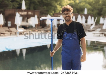 Pool cleaner in uniform, smiling while holding a cleaning net at the poolside, preparing to begin a productive workday