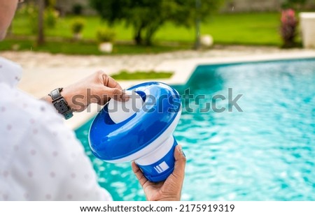 Pool float and chlorine tablets for pool maintenance. Hands holding a pool chlorine dispenser.
