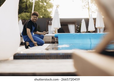 Pool maintenance worker checking the automatic pool covering system with a smartphone, ensuring optimal functionality and safety during summer days