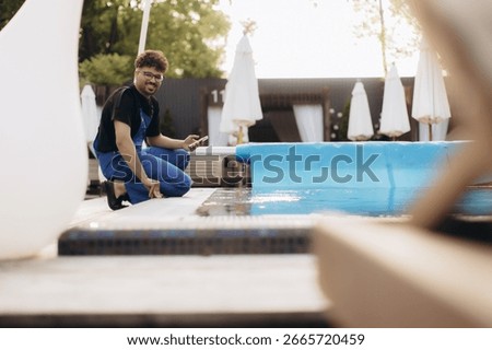 Pool maintenance worker checking the automatic pool covering system with a smartphone, ensuring optimal functionality and safety during summer days