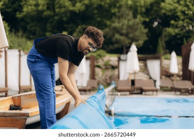 Pool maintenance worker rolling up a pool cover at a resort, ensuring cleanliness and safety for guests enjoying summer leisure by the blue water