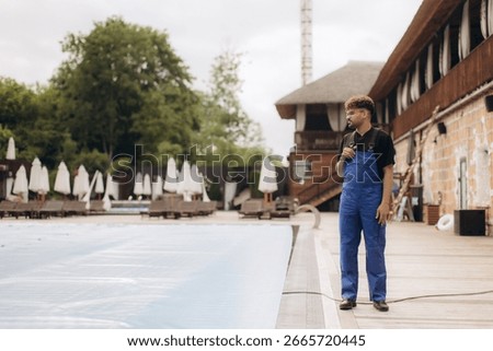 Pool maintenance worker in uniform inspecting a covered outdoor pool as part of the closing process, ensuring safety and care for winter preparation