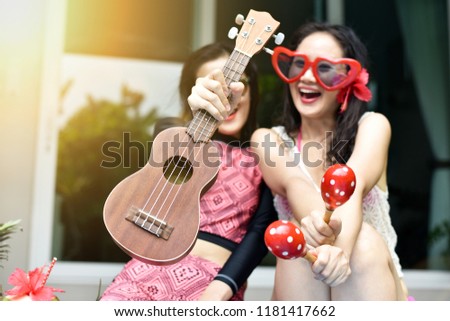 Pool party, Happy women enjoy playing music instrument by the swimming pool, Girlfriends in bikini smile and laughing, Fresh tropical fruit, Summer holiday vacation.