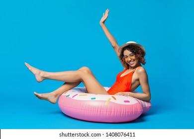 Pool party. Positive african american girl sitting on big inflatable ring, ready to swim, blue studio background with empty space