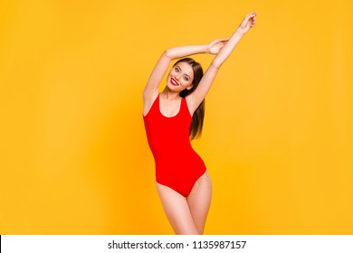 It is pool party time! Charming brunette in red swimsuits with hands up having fun stand isolated on vivid yellow background