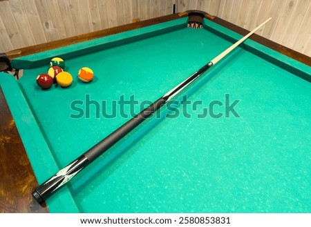 A pool table with a black pool cue and three balls on it. Scene is relaxed and leisurely