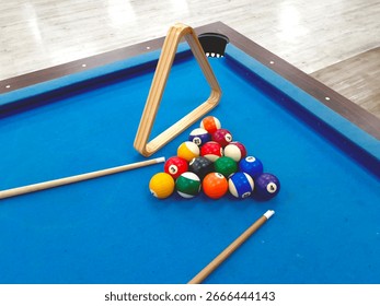 Pool table setting with billiard balls, cue sticks, and wooden triangle rack.