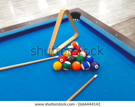 Pool table setting with billiard balls, cue sticks, and wooden triangle rack.
