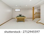 Pool table sits in a large, empty room. The room is mostly white, with a few brown accents. Scene is calm and inviting, as the pool table is a focal point of the room