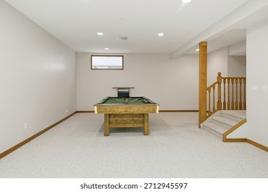 Pool table sits in a large, empty room. The room is mostly white, with a few brown accents. Scene is calm and inviting, as the pool table is a focal point of the room