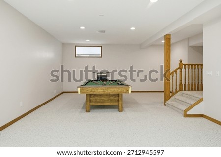 Pool table sits in a large, empty room. The room is mostly white, with a few brown accents. Scene is calm and inviting, as the pool table is a focal point of the room