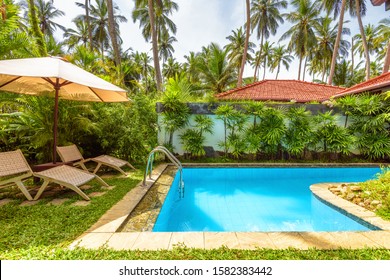 Pool With Umbrella And Beach Beds In Tropical Hotel Or Home Back Yard. Landscaping Of Courtyard, Scenery Of Nice Swimming Pool In Residential House Backyard. Beautiful Palm Garden For Relax In Resort