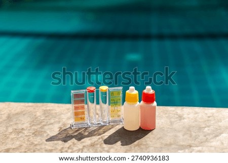 Pool water test kit with pH and chlorine scale and reagent bottles on pool edge, swimming pool maintenance and water quality control concept. High quality photo