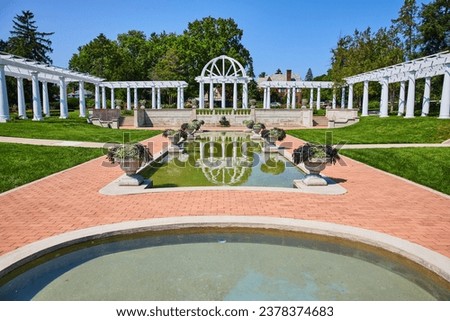 Pools of water with stone flowerpots leading to white pergola and trellises at end of stone path