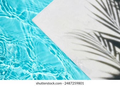 Poolside Serenity. Shadow of a palm tree on a white surface next to a clear blue swimming pool.