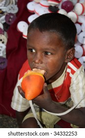 A Poor Beggar Boy In India Playing With His Toy, On The Streetside. He Is Sick With Fever, Having Cold And Running Nose.